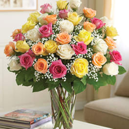 Mixed bouquet of roses in pink, yellow, peach, and white in a glass vase