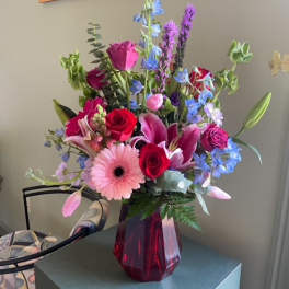Mixed bouquet of roses, lilies, and blue flowers in a red vase