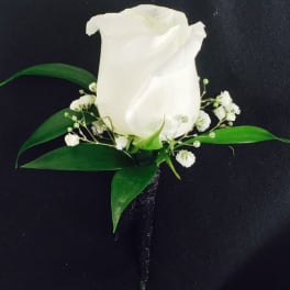 White rose boutonniere with small white filler flowers and green leaves