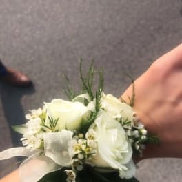 White rose wrist corsage with small white blooms and sheer ribbon on a person's wrist