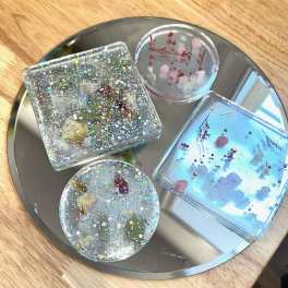 Four resin coasters with embedded dried flowers and glitter on a round tray