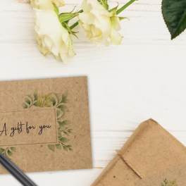 White roses with gift cards, wrapped packages, and a pen on a white surface