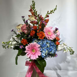 Mixed bouquet with pink gerberas, orange roses, blue hydrangea, and white blooms in a vase