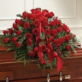 Red rose casket spray with ribbon accents on a wooden casket