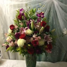 Tall bouquet of red roses, pink lilies, and purple orchids in a glass vase