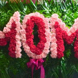 Pink and red floral arrangement spelling MOM with a ribbon bow