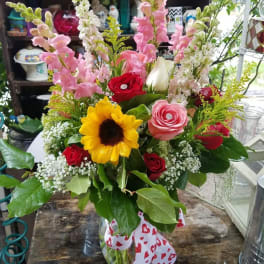 Mixed bouquet in a glass vase with roses, sunflower, and pink snapdragons