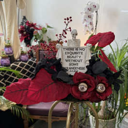 Halloween floral arrangement with red roses and a skeleton holding a quote sign