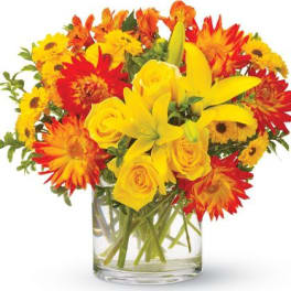 Bright bouquet of yellow lilies and roses with orange and yellow mums in a clear glass vase
