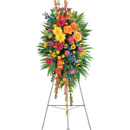 Tall standing floral spray with bright yellow, orange, pink, and blue flowers on a metal easel.