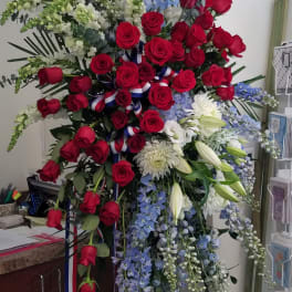 Tall standing spray with red roses, white lilies and mums, blue delphinium, and patriotic ribbon accents