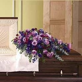Purple and pink mixed flower casket spray draped over a wooden casket