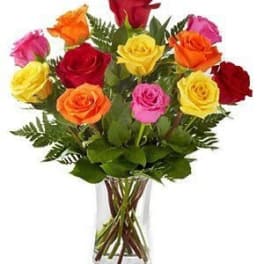 Mixed bouquet of red, yellow, orange, and pink roses arranged in a clear glass vase