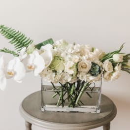 White orchid and cream floral arrangement in a clear rectangular vase