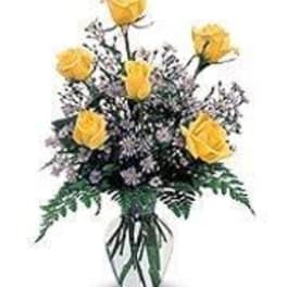 Arrangement of yellow roses and small purple flowers in a clear glass vase