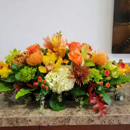 Low floral centerpiece with orange roses, yellow orchids, and white hydrangea