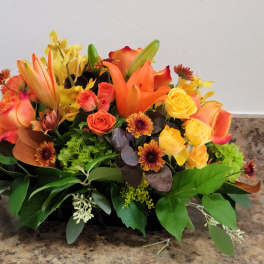 Orange and yellow floral arrangement with roses and lilies in a low container