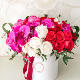 Pink and red floral arrangement in a white hat box with ribbon