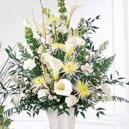 Tall white arrangement with calla lilies and chrysanthemums in a white urn.