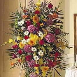Tall standing spray of mixed bright flowers on an easel with a yellow ribbon