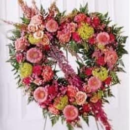 Standing open-heart wreath of pink and peach flowers with green accents on a metal easel.