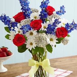 Bouquet of red roses, white daisies, and blue flowers in a glass vase
