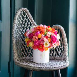 Bright mixed bouquet in a white cylindrical box on a woven chair