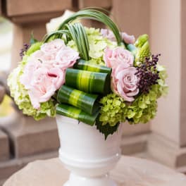 Pink roses and green hydrangeas arranged in a white urn