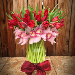 Bouquet of red tulips and pink orchids in a glass vase with a red bow