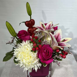 Pink roses and white lilies in a square glass vase with a white chrysanthemum
