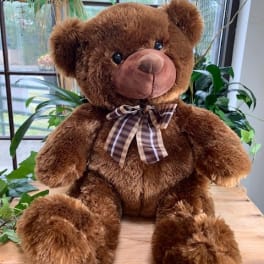 Brown teddy bear with a plaid bow sitting on a wooden table