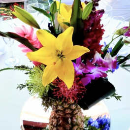 Tropical flower arrangement in a pineapple vase with yellow lilies and purple orchids