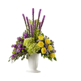 Purple and yellow floral arrangement in a white pedestal vase