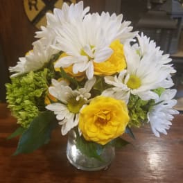 Yellow roses and white daisies arranged in a clear glass vase