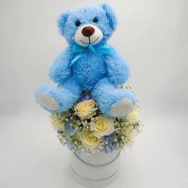 Blue teddy bear sitting on a bouquet in a white hatbox