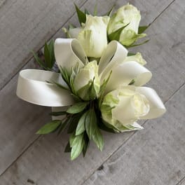 White rose boutonniere with green leaves and a white ribbon