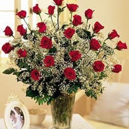 Tall arrangement of red roses with white filler flowers in a clear glass vase