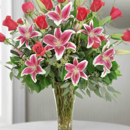 Tall glass vase of red roses and pink lilies arranged in a lush mixed bouquet