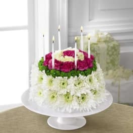Round floral arrangement styled like a birthday cake with candles on a white stand