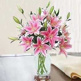 Pink lily arrangement with buds in a clear glass vase on a table
