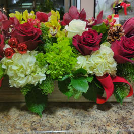 Rectangular holiday centerpiece with red roses, white hydrangeas, green mums, orchids, and evergreens in a wooden box.