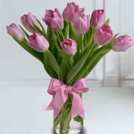 Pink tulips in a clear glass vase tied with a pink ribbon bow