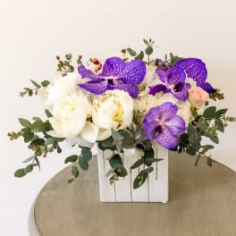 White and purple floral arrangement in a white wooden box