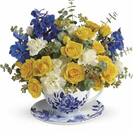 Yellow and blue flower arrangement in a teacup with saucer