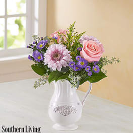 Pink and purple flowers arranged in a white pitcher vase