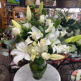 Tall arrangement of white lilies, roses, and hydrangeas in a clear glass vase