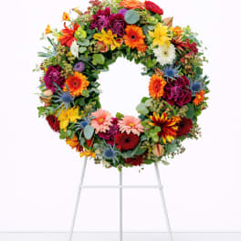 Bright multicolor floral wreath displayed on a white metal stand