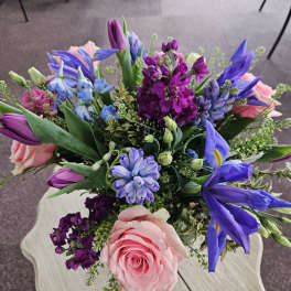 Colorful bouquet with pink roses, purple stock, tulips, blue iris and hyacinth on a light wood table