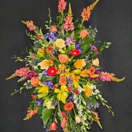 Tall standing spray of yellow lilies, orange roses, and bright mixed flowers on a black background