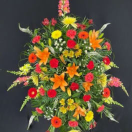 Tall standing spray of orange lilies, red carnations, and mixed bright flowers on an easel
